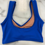 A royal blue dance bra with a scoop neckline, laid flat on a white marble surface. The interior lining is a peachy-pink color.