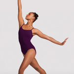 A female dancer in a deep purple leotard poses in a graceful ballet position against a light gray studio background.