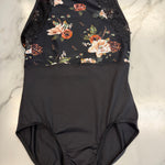A black one-piece leotard with a floral print bodice and lace trim, laid flat on a white marble surface.