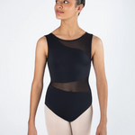 A female dancer wearing a black sleeveless leotard with sheer mesh panels and light pink tights, standing against a plain white studio background.