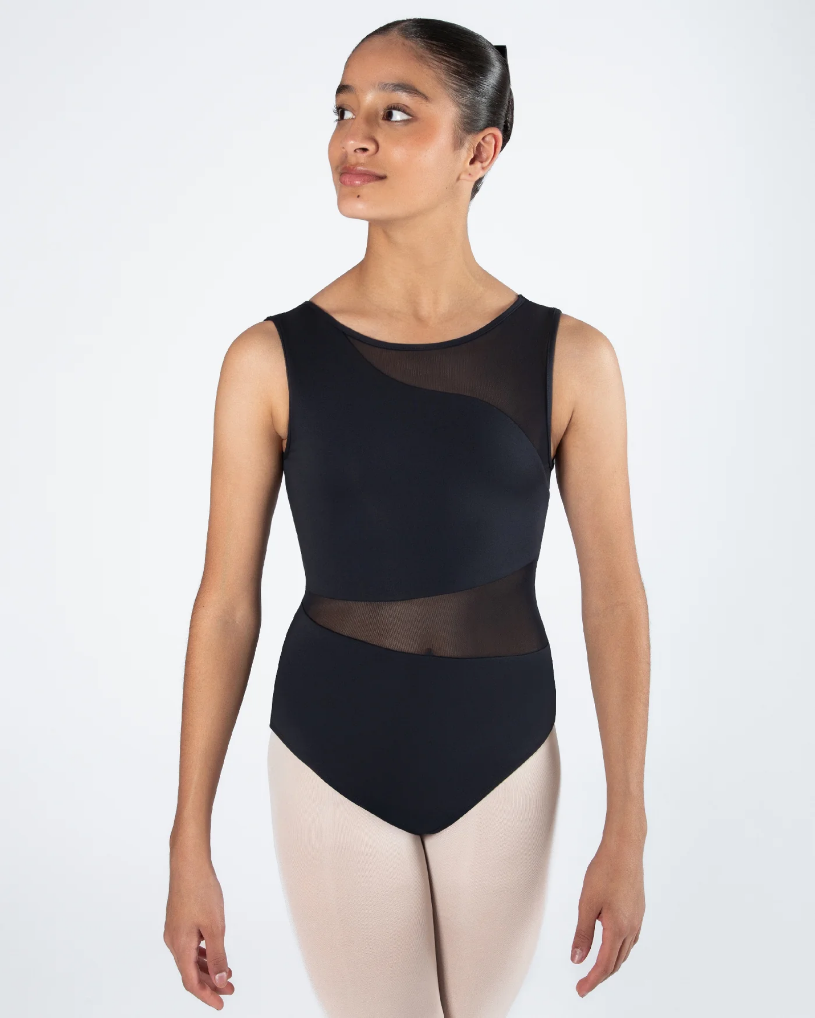 A female dancer wearing a black sleeveless leotard with sheer mesh panels and light pink tights, standing against a plain white studio background.