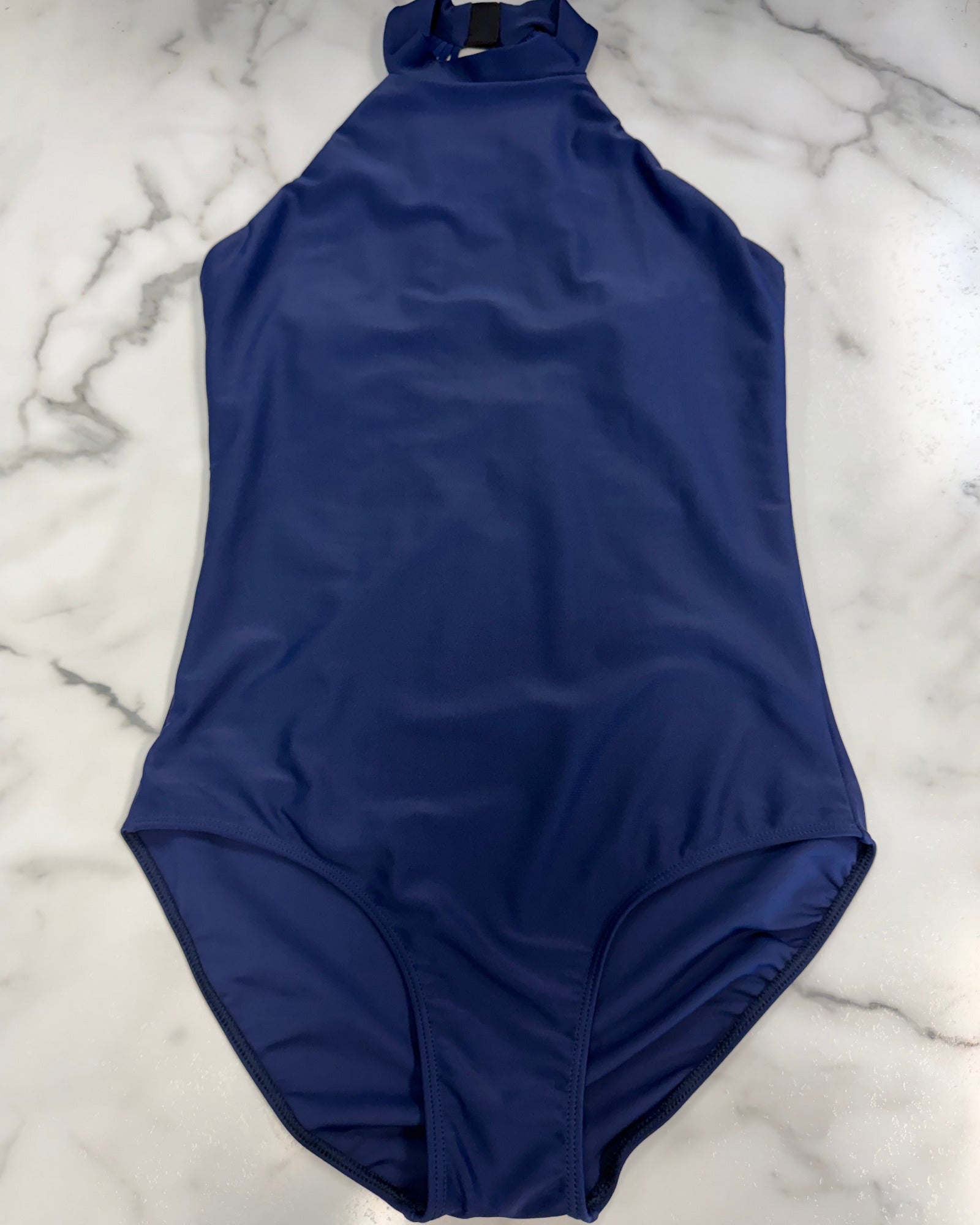 A royal blue sleeveless one-piece leotard with a mock neck, laid flat on a white marble background.