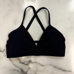 A navy triangle dance top with crisscrossing back straps, laid flat on a white marble surface.