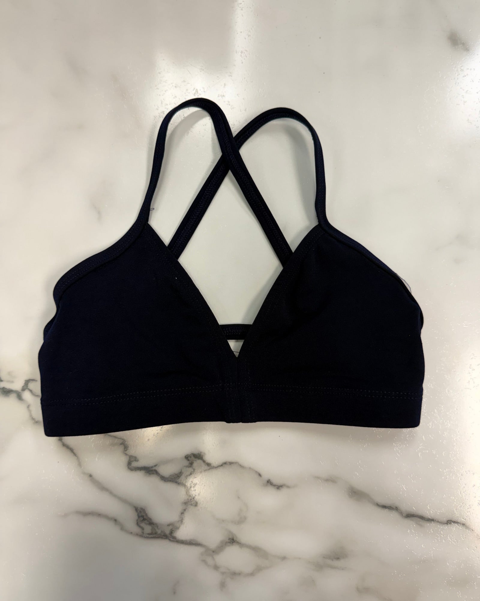 A navy triangle dance top with crisscrossing back straps, laid flat on a white marble surface.