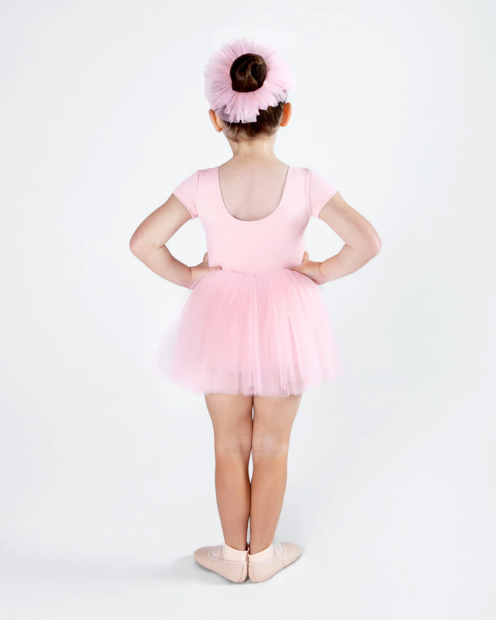 Young girl in a pink ballet outfit with a tutu and headband on a white background