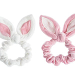 Two plush bunny-ear scrunchies on a white background, one white with a pink inner ear and one pink with a white inner ear.