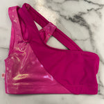 A bright pink dance bra with a shiny metallic magenta panel and solid pink side panels, laid flat on a white marble surface.