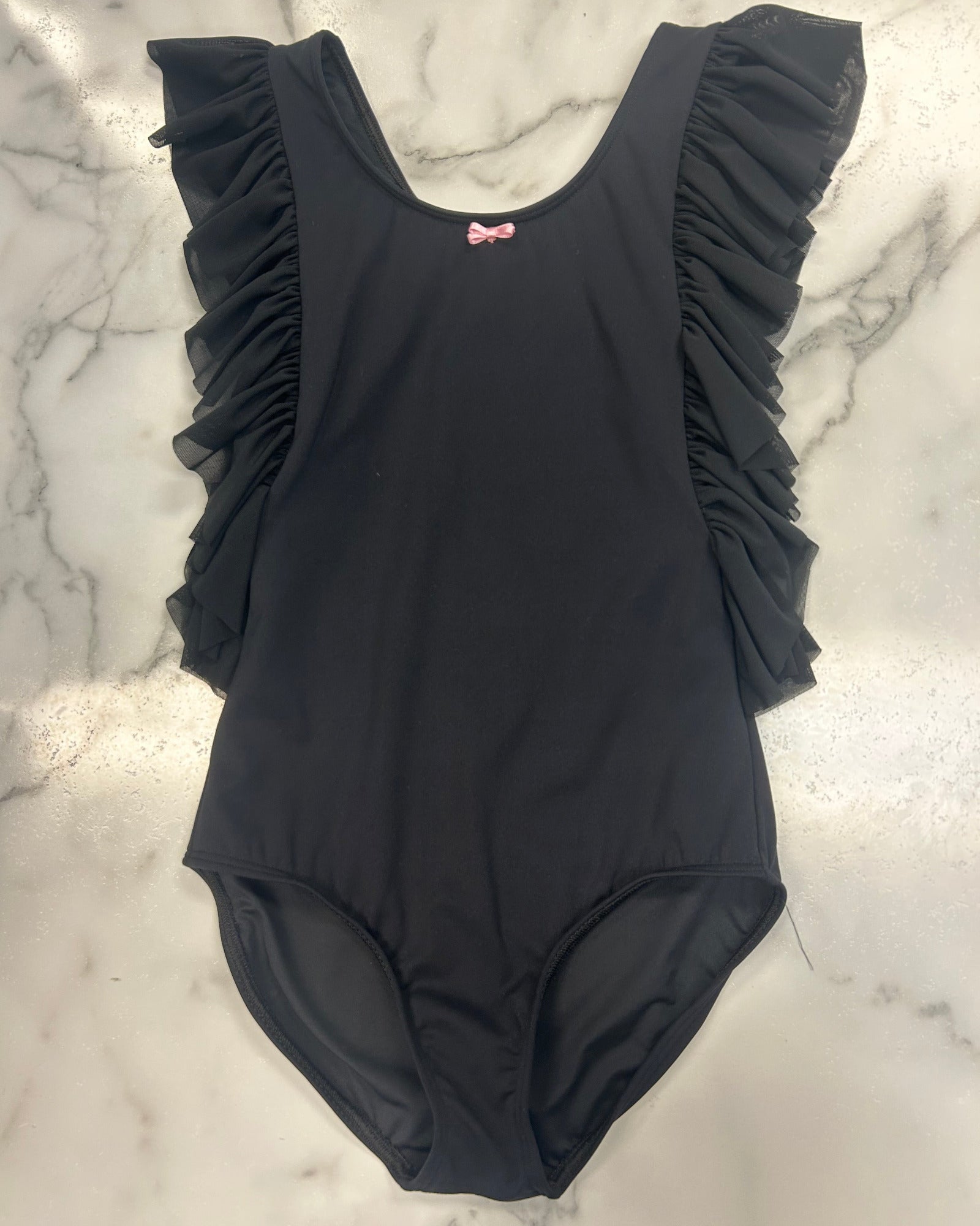 A black one-piece leotard with ruffled shoulder details and a small pink bow accent at the neckline, laid flat on a white marble surface.