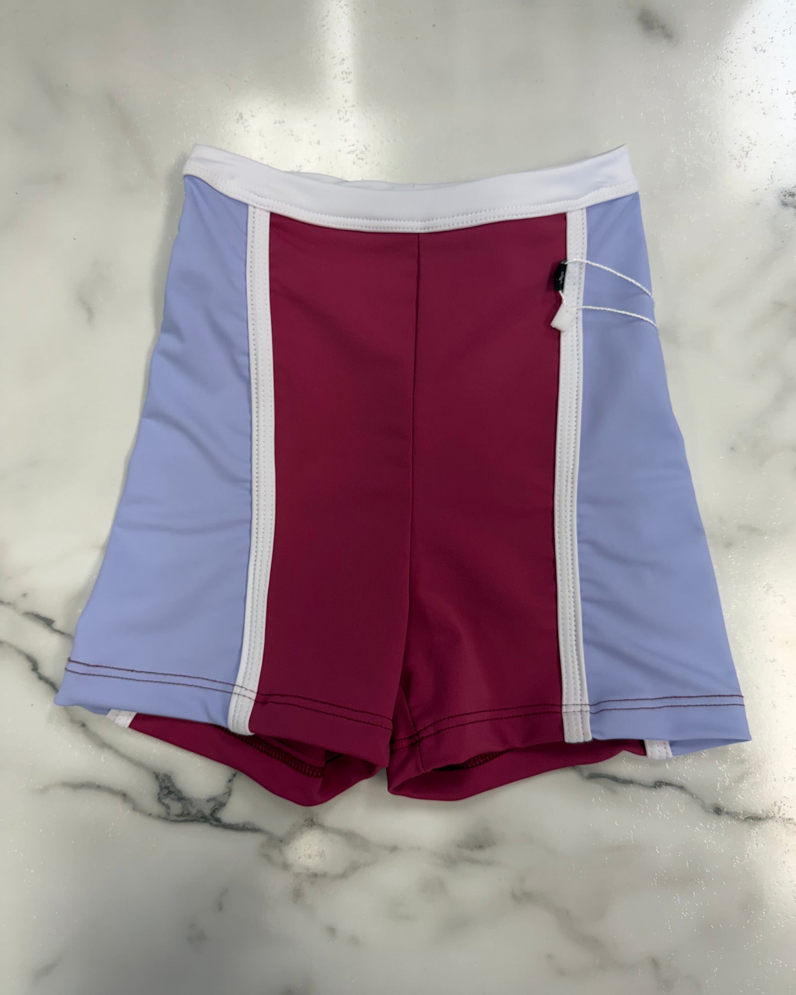 Colorblock dance shorts in light purple, burgundy, and white, laid flat on a white marble surface.