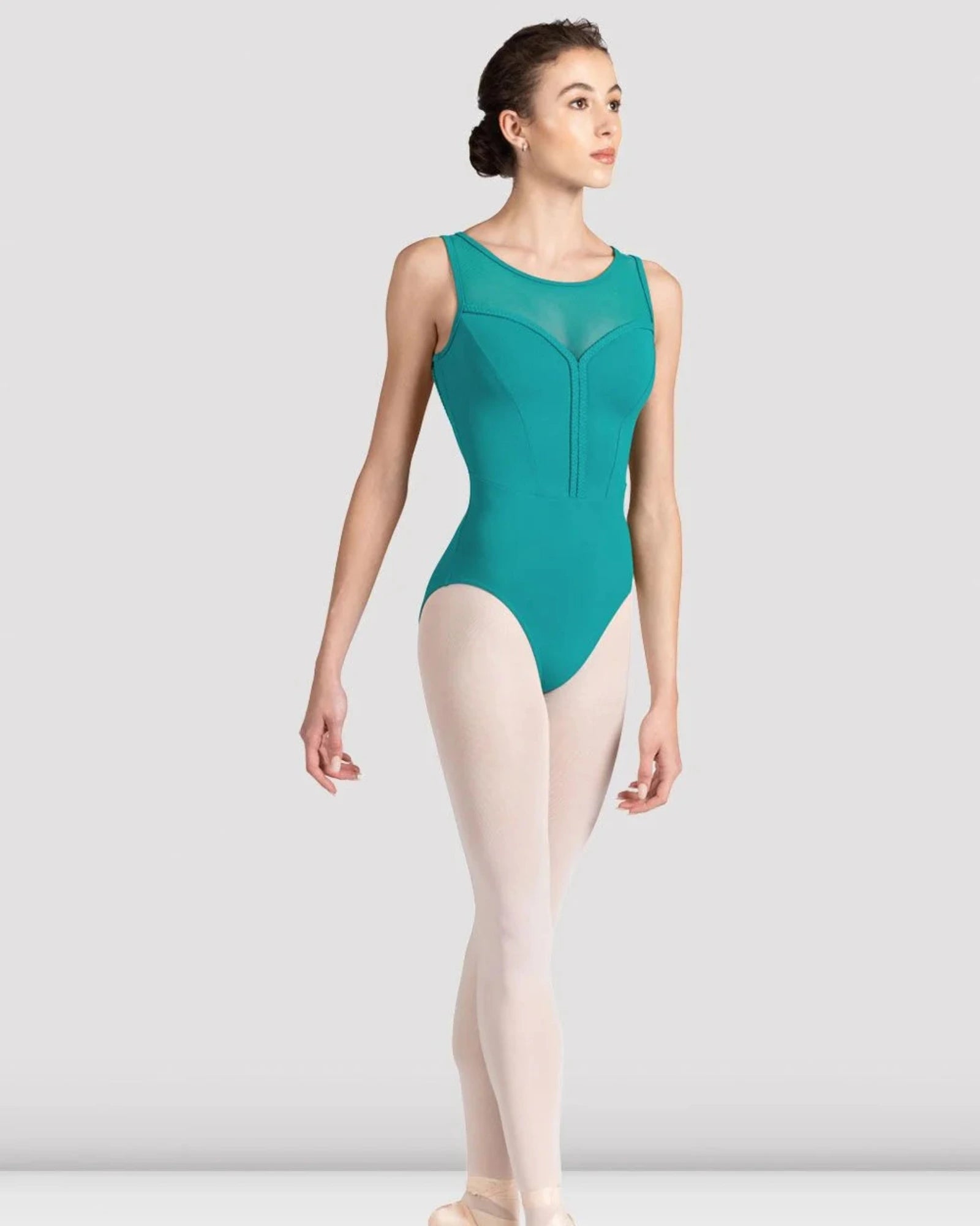 A female dancer in a sleeveless teal leotard, pink tights, and pointe shoes, standing en pointe against a light gray studio background.