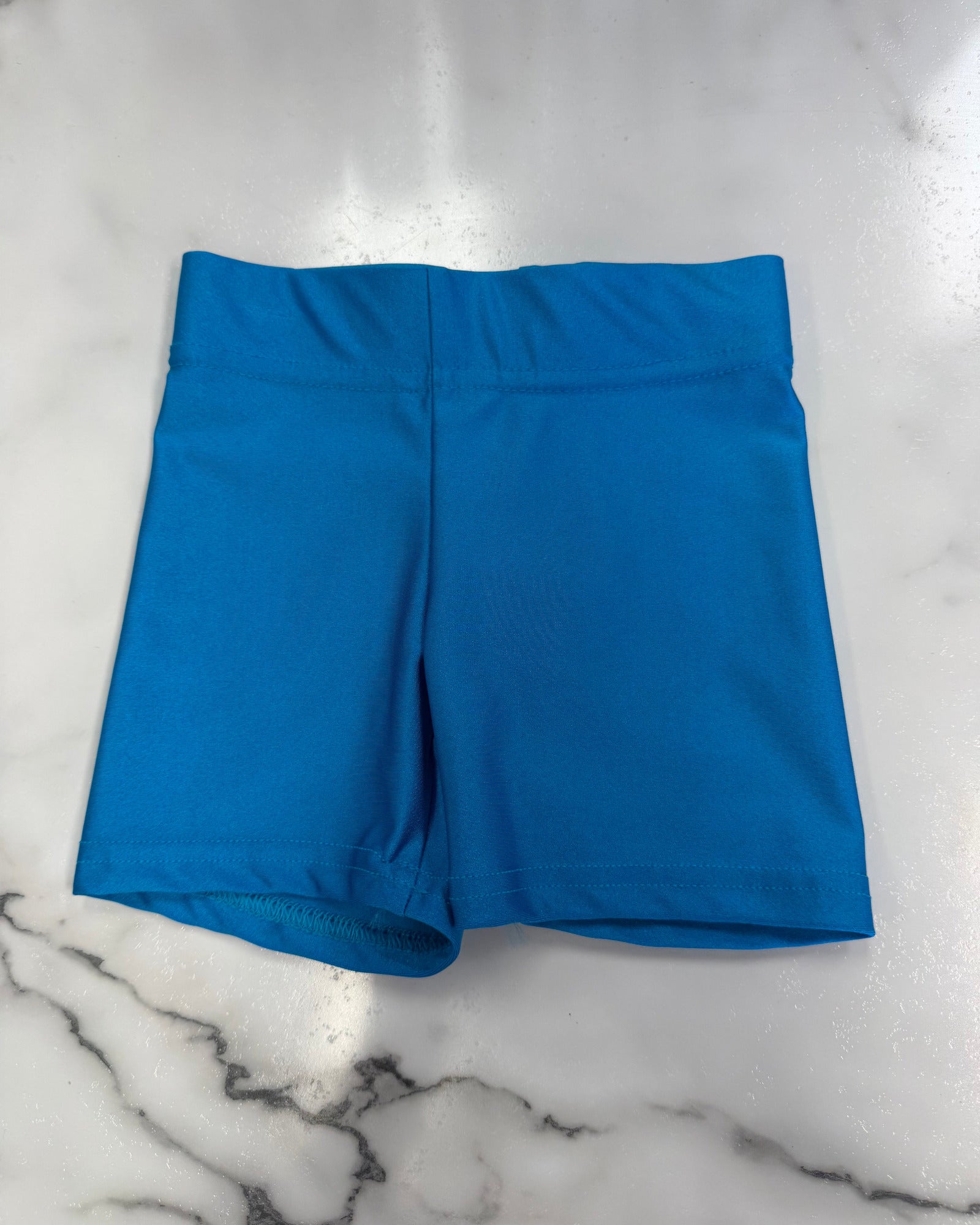 A pair of bright blue athletic shorts laid flat on a white marble surface.