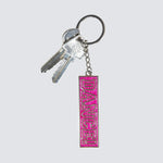 A pink rectangular keychain with the word 'DANCE' in raised lettering, attached to a silver metal keyring with two keys, on a light gray background.
