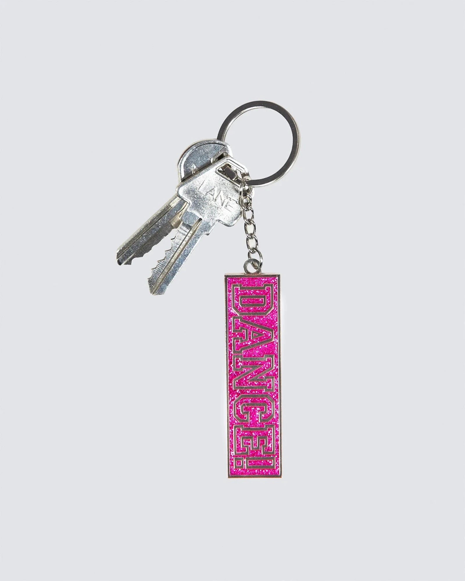 A pink rectangular keychain with the word 'DANCE' in raised lettering, attached to a silver metal keyring with two keys, on a light gray background.