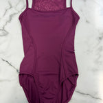A plum-colored leotard with thin shoulder straps and a textured patterned inner neckline, laid flat on a white marble background.