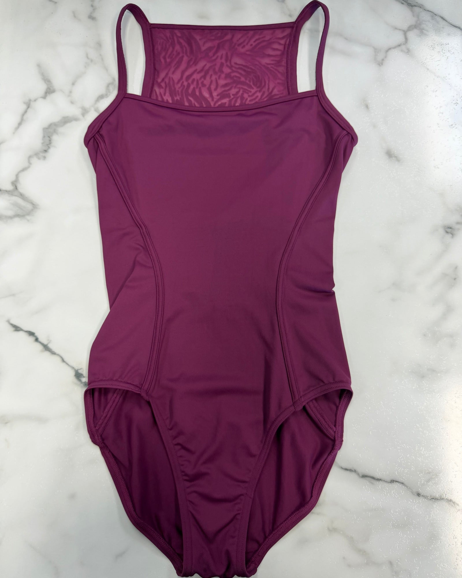 A plum-colored leotard with thin shoulder straps and a textured patterned inner neckline, laid flat on a white marble background.