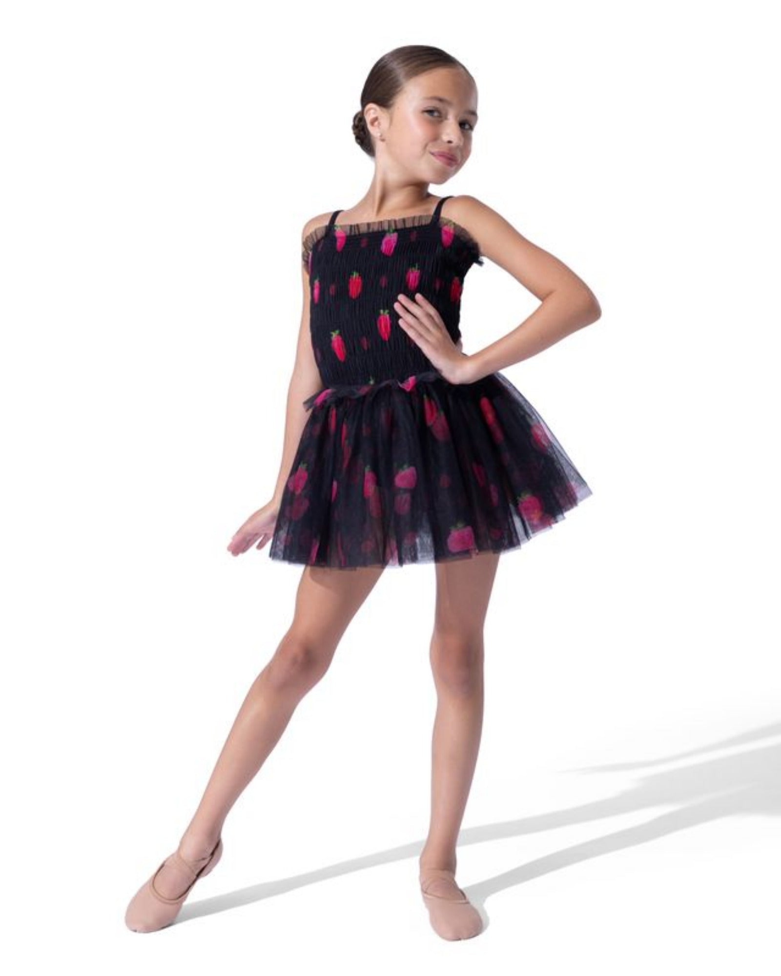 A young girl dancer wearing a black tulle tutu dress with a red strawberry pattern, posed against a solid white studio background.