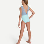 A young girl modeling a two-tone leotard from the back, featuring a light blue upper back and shoulder straps with a light mint green lower body, set against a plain light gray studio background.