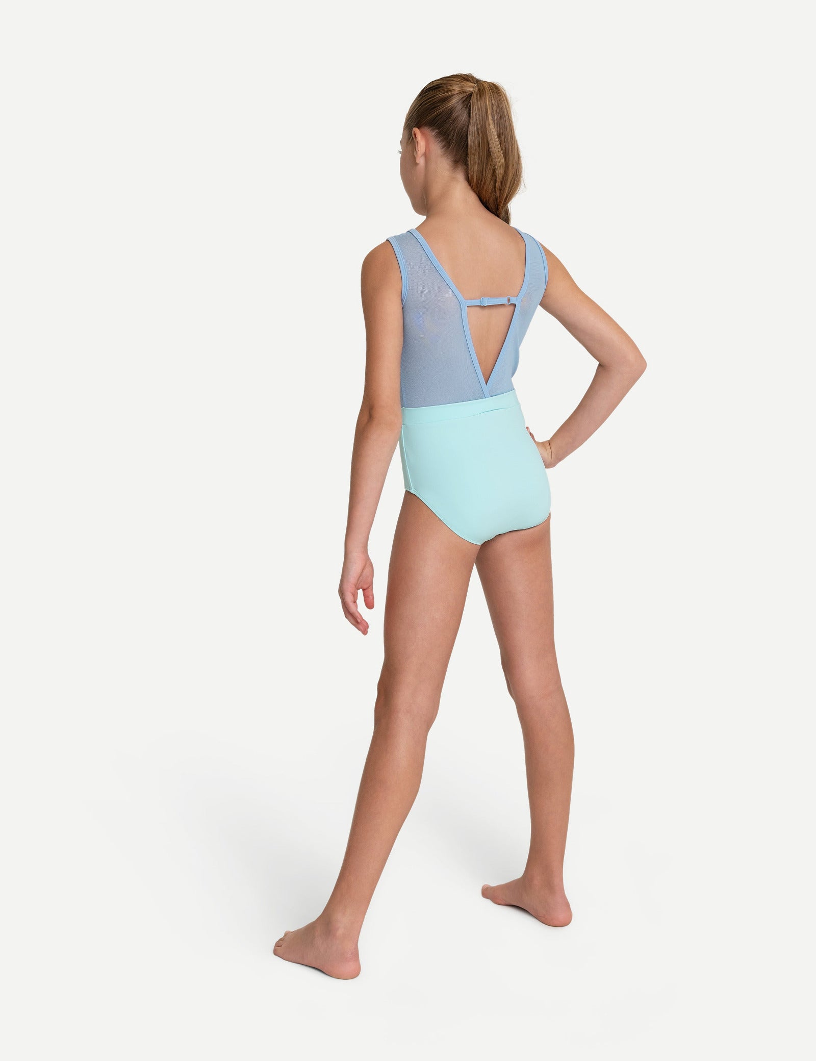 A young girl modeling a two-tone leotard from the back, featuring a light blue upper back and shoulder straps with a light mint green lower body, set against a plain light gray studio background.