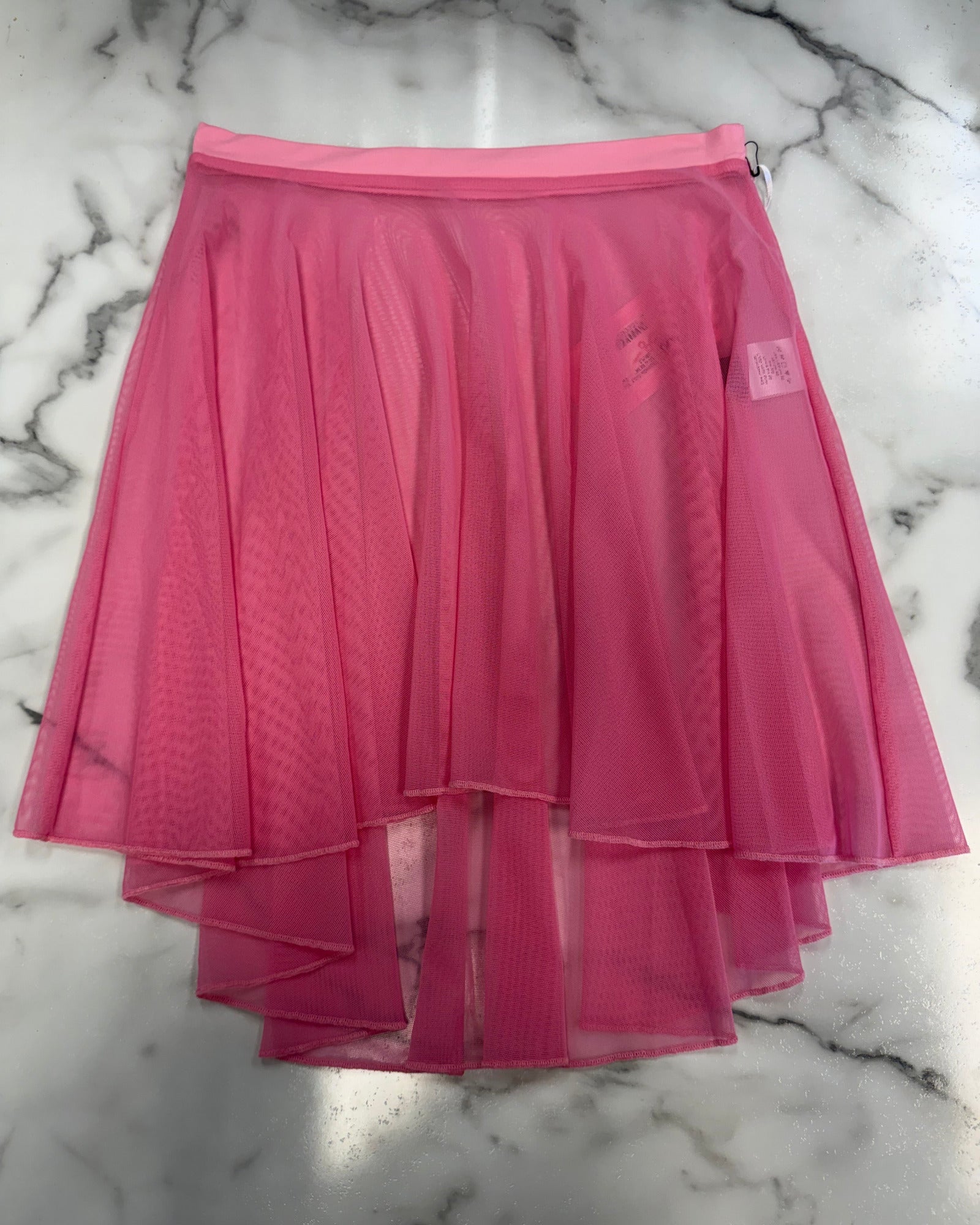 A bright pink mesh high-low dance skirt with a high low hem, laid flat on a white and gray marble surface.