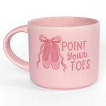 A light pink ceramic mug with a matching pink handle, featuring a graphic of ballet slippers and the text 'POINT YOUR TOES' in pink lettering.