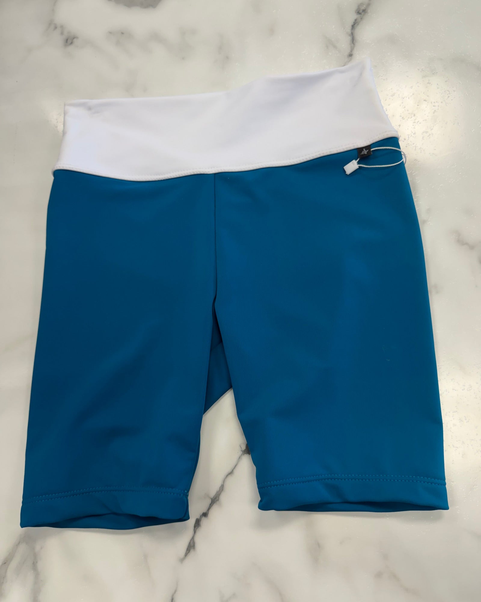 Blue and white athletic biker shorts laid flat on a white marble surface.