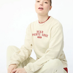 Person wearing a cream sweatshirt with text and pants, sitting on a white background