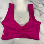 A bright magenta pink dance bra with a ruched front and wide shoulder straps, laid flat on a white marble surface.