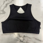 A black athletic dance bra top with a keyhole cutout at the back, laid flat on a white marble surface.