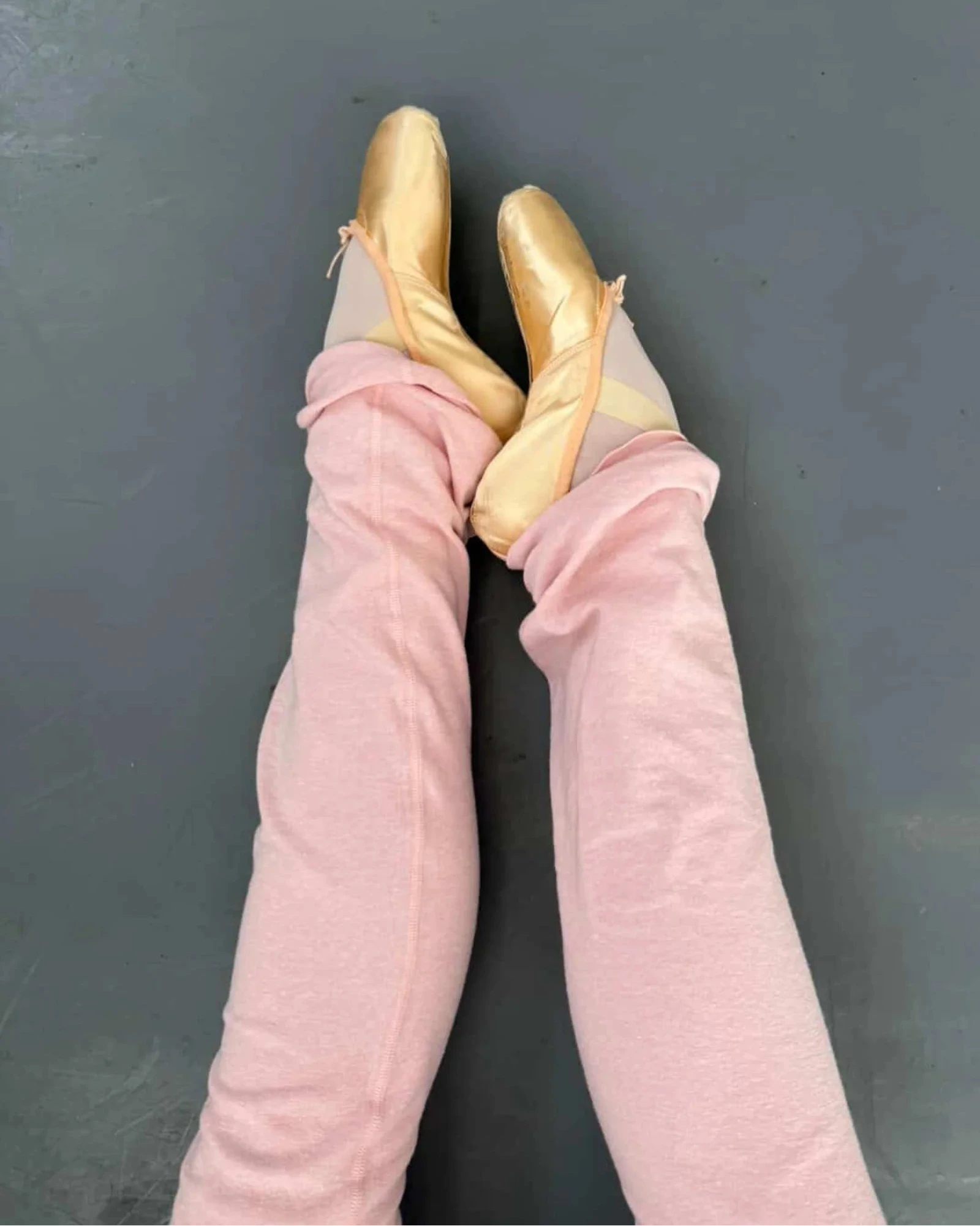 Pointe shoes with pink legwarmers against a dark background