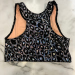 A sleeveless athletic crop top with a black leopard print pattern featuring iridescent blue and pink highlights, laid flat on a white marble surface.