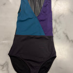 A color-blocked leotard laid flat on a white marble surface. The top portion features diagonal panels of teal blue, purple, and a sheer dark gray mesh insert, while the bottom is a solid dark charcoal black.