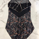 A leotard with a black mesh and solid black upper section, featuring a multicolor paisley pattern on a black base on the lower half, laid flat on a white marble surface.