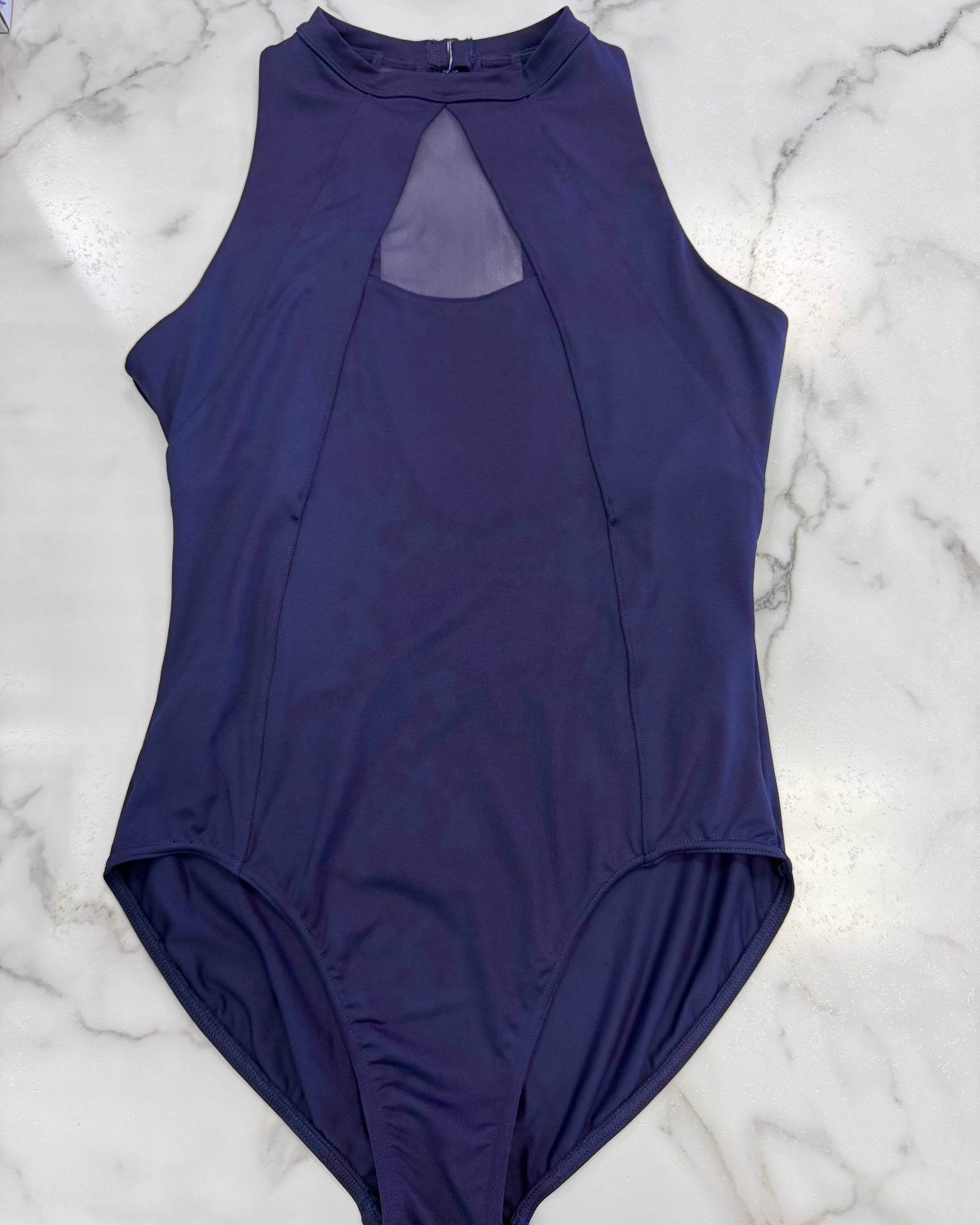 A sleeveless dark purple leotard laid flat on a white marble surface, featuring a high mock neck with a keyhole cutout at the back.