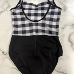 A leotard laid flat on a white marble surface. The top half features a black and white gingham check pattern with black straps, and the bottom half is solid black.