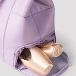 Purple ballet shoe bag with ballet shoes inside on a light gray background
