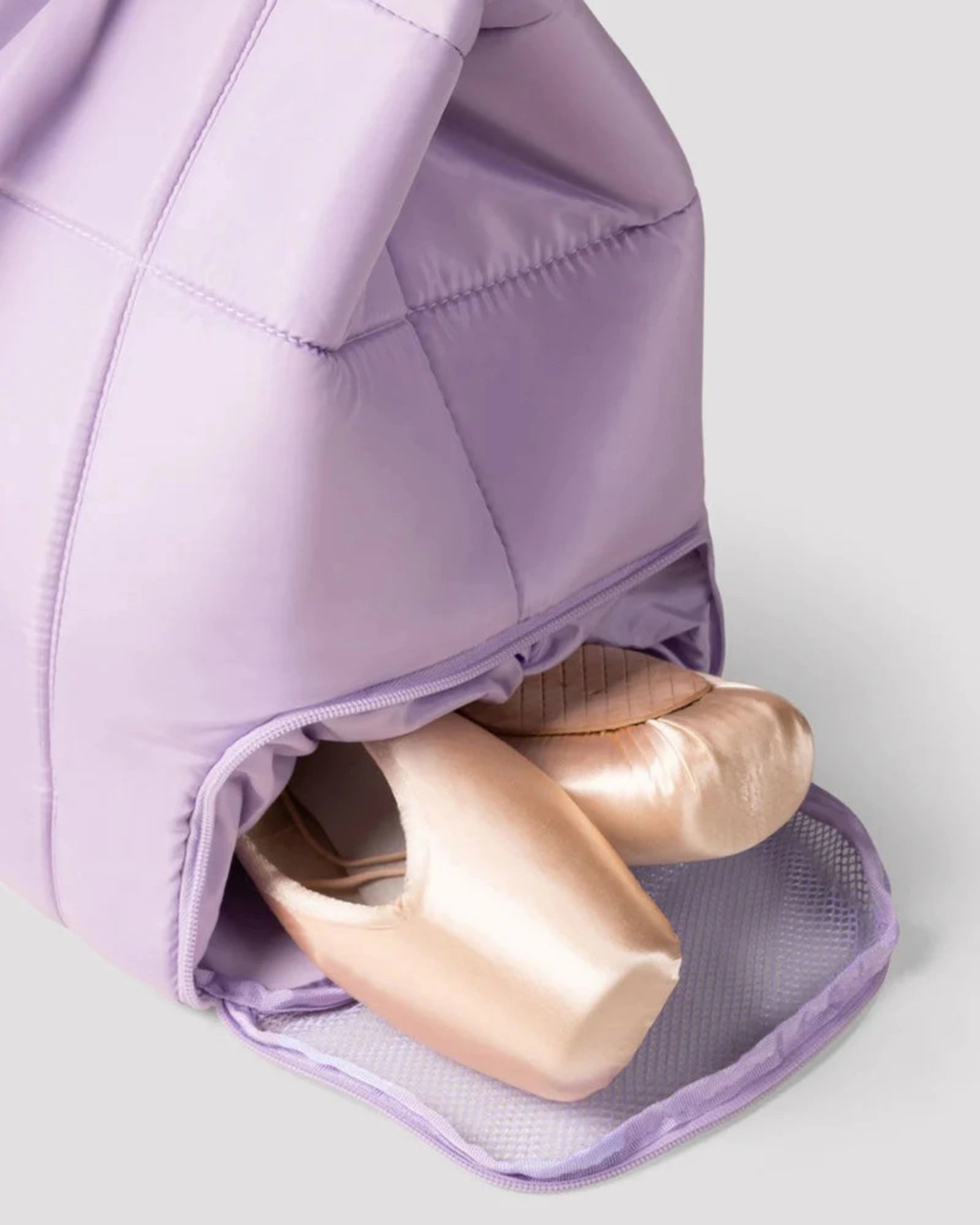 Purple ballet shoe bag with ballet shoes inside on a light gray background