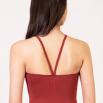 Rust red halter-neck leotard shown from the back on a model, featuring thin crossover straps and a clean silhouette against a plain white background.
