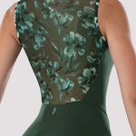 A close-up back view of a woman wearing a one-piece swimsuit or leotard in dark green, featuring a sheer floral mesh back panel with teal and green floral print over a dark olive background.