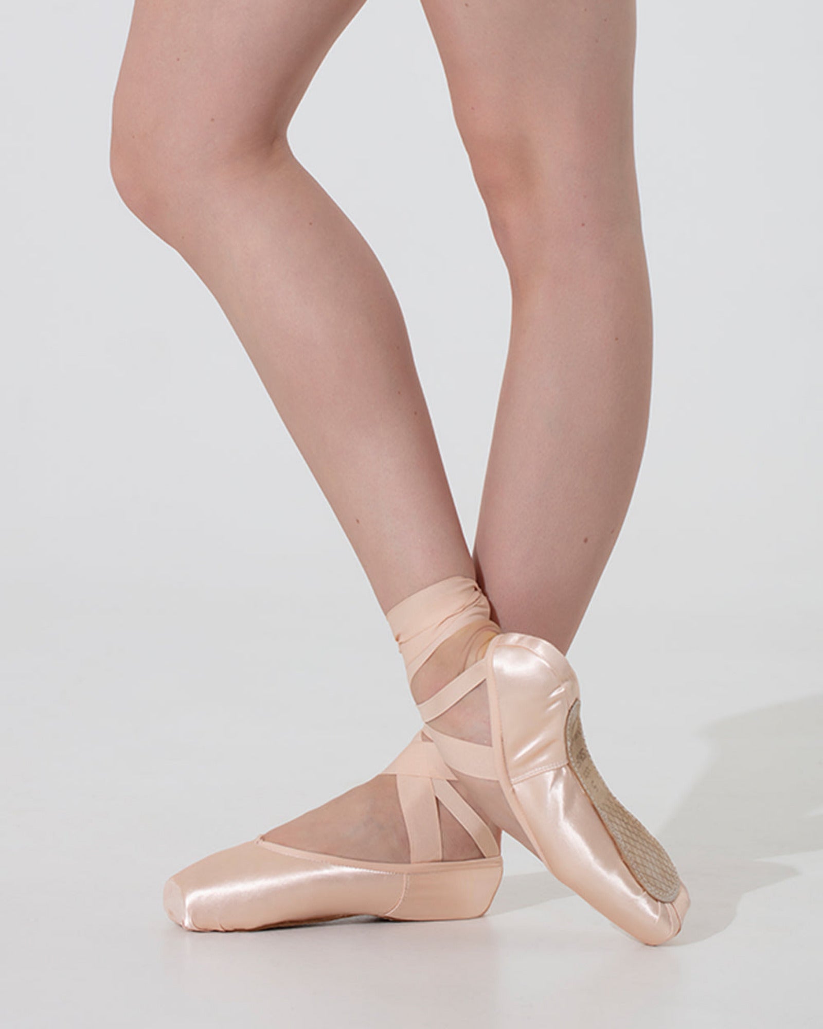 Ballet shoes worn with sheer tights on a plain background