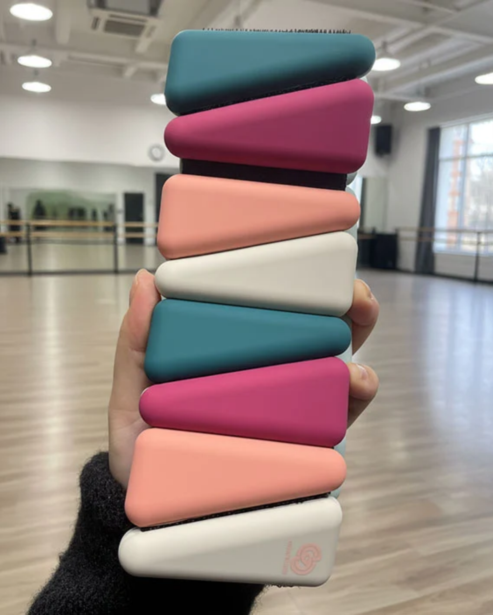 Stack of colorful leg weights held in a hand with a dance studio background