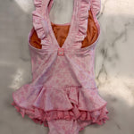 A pink baby girl's one-piece leotard with ruffled straps and a ruffled hem, featuring a light pink strawberry pattern and a bright orange inner lining, laid flat on a white marble surface.