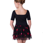 A young girl is shown from the back wearing a black short-sleeve dress with a square neckline and a tulle skirt featuring a red strawberry pattern