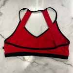 A red crop top with black trim and a racerback-style back strap design, laid flat on a white marble surface.