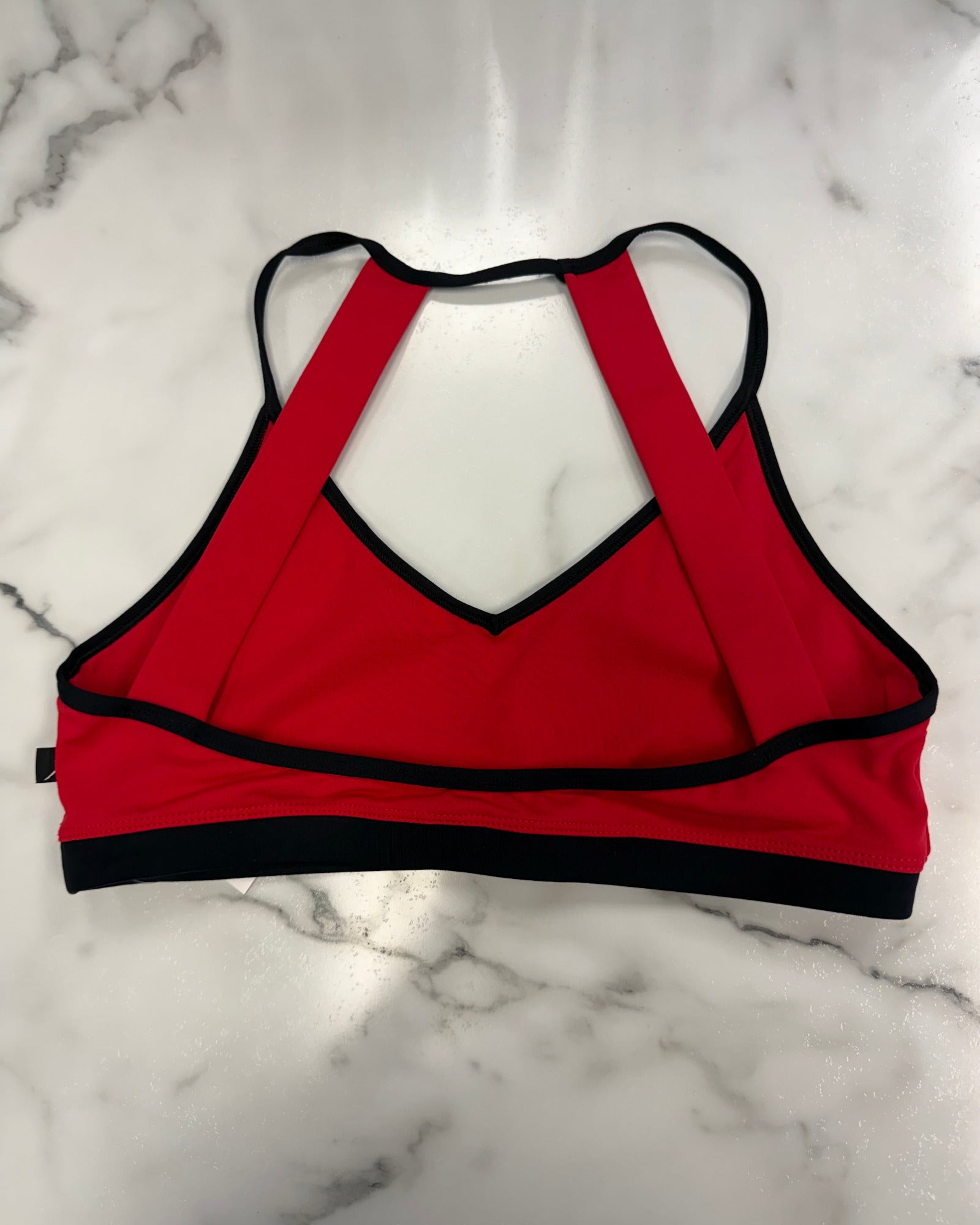 A red crop top with black trim and a racerback-style back strap design, laid flat on a white marble surface.