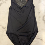 A black sleeveless leotard with a V-neckline and a textured mesh chest panel, laid flat on a white marble surface.