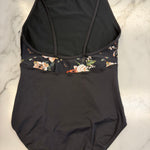 A black one-piece leotard with a floral patterned underbust band, laid flat on a white marble surface.