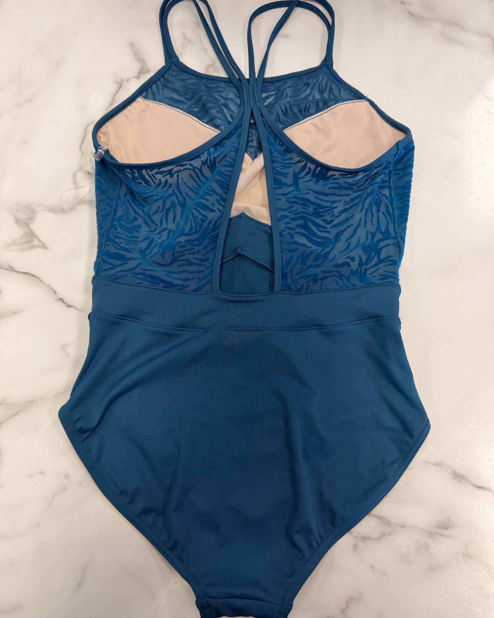 A blue leotard with a zebra textured pattern on the upper section, beige lining, and a back keyhole detail, laid flat on a white marble surface.
