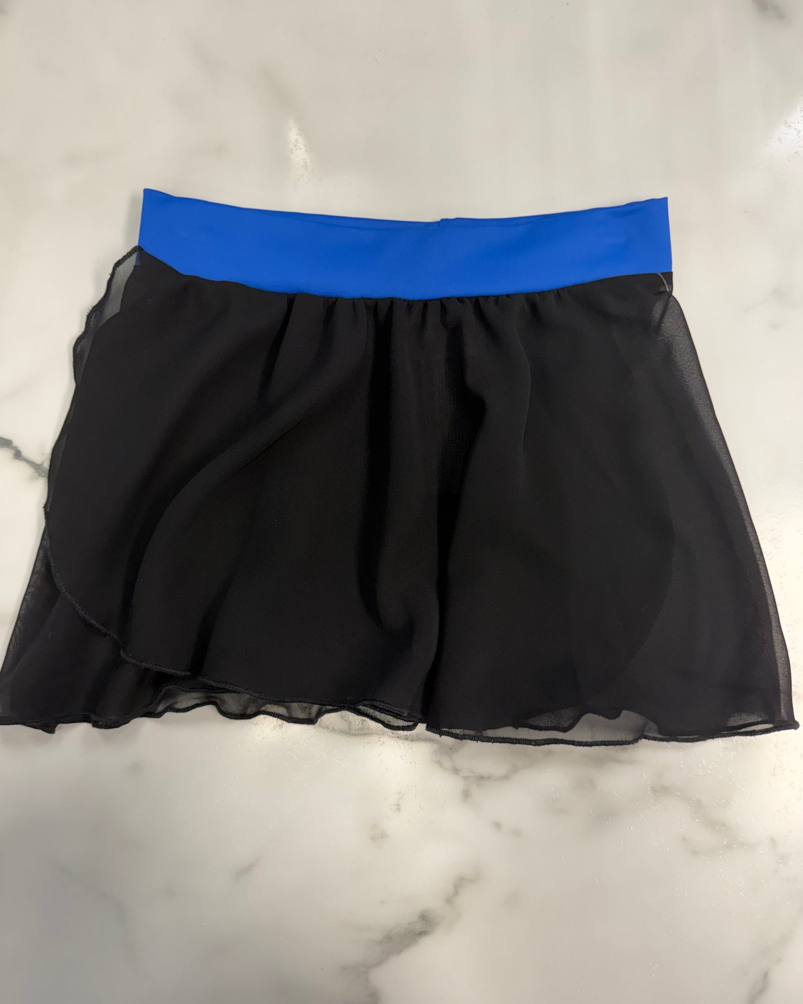 A black sheer mesh skirt with a bright blue elastic waistband, laid flat on a white marble surface.