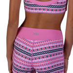 A model is shown from the back wearing a matching pink dance wear set with a Fair Isle pattern. The set includes a sports bra and shorts with a solid pink waistband and a geometric pattern in pink, green, and white.