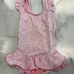 A pink one-piece baby leotard with a delicate pink floral and leaf pattern, featuring ruffled shoulder straps and a ruffled hem, laid flat on a white marble surface.